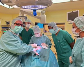 Ein Team von Chirurgen in OP-Kleidung führt eine Operation durch, während sie sich auf den Patienten konzentrieren.