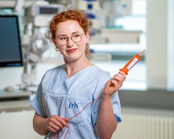 Eine Krankenschwester in blauer Arbeitskleidung hält ein medizinisches Gerät in der Hand und steht in einem modernen Krankenhausumfeld.
