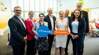 Eine Gruppe von Personen steht zusammen und hält ein Schild mit der Aufschrift "SRH Gesundheit" und "SRH University".