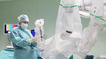 Eine Person in medizinischer Kleidung bedient einen chirurgischen Roboter, der in einer Operationsumgebung vorbereitet wird.